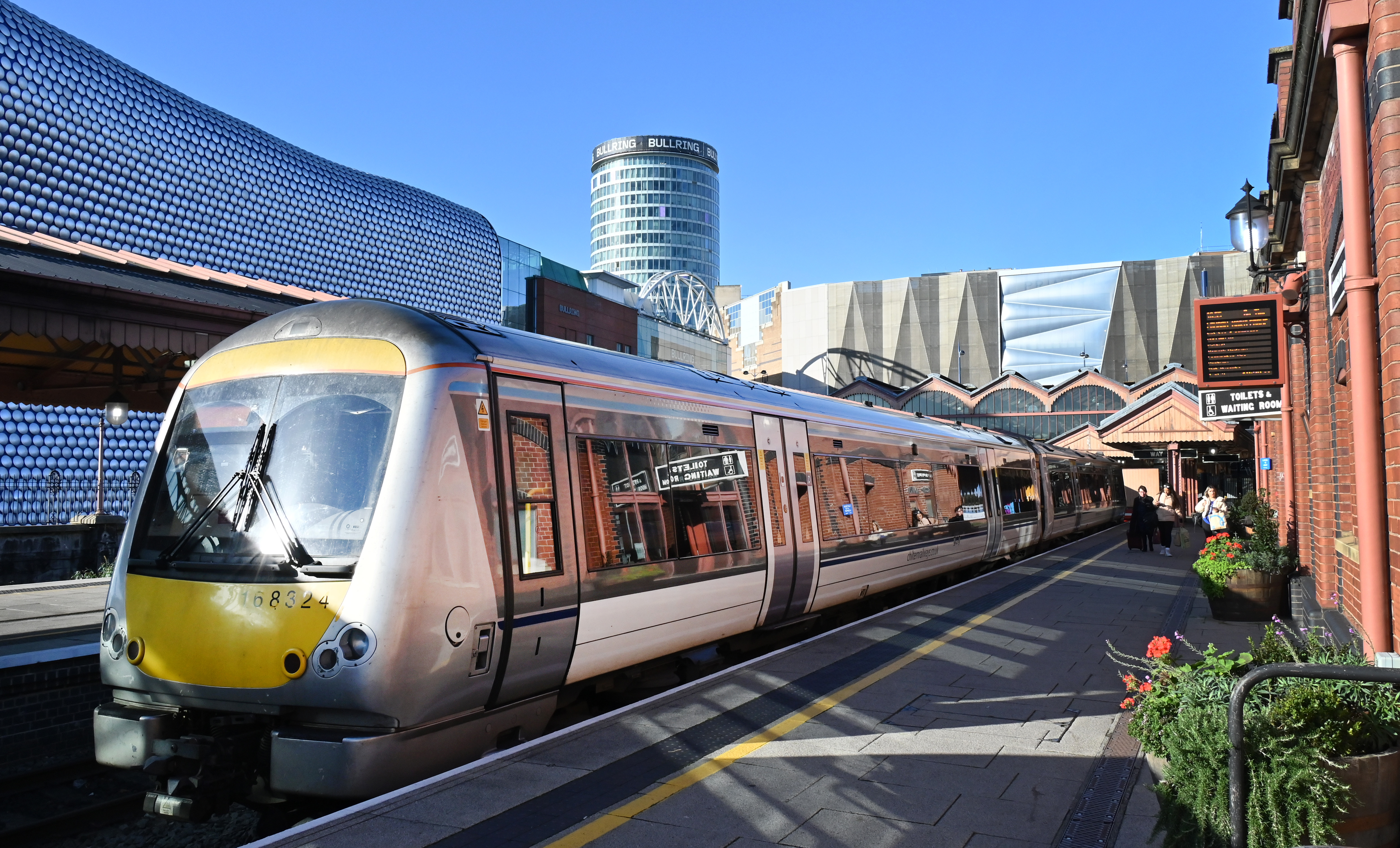 Photo of a train pulled in at Birmingham's Moor Street station. The Bullring and Rotunda can be seen in the background. 